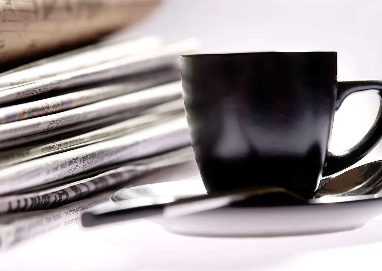 Black coffee cup in front of a stack of newspapers